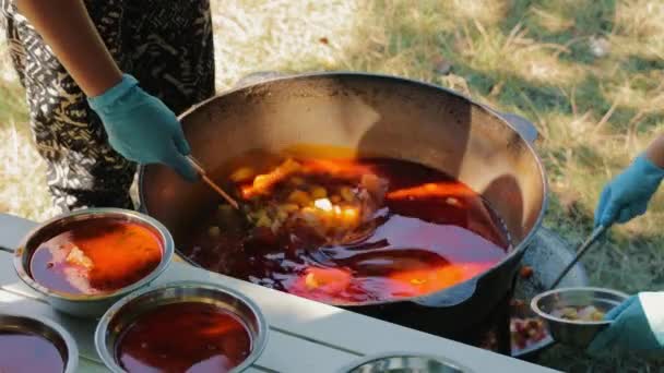 在室外用大锅大锅炖肉或罗宋汤进行特写 而女人们则用厨房里的小勺把汤倒进金属盘子里 野营季节 — 图库视频影像
