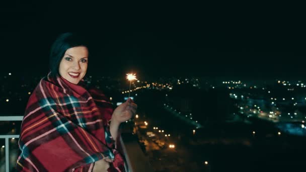 在夜城的背景下 一个快乐的女人手里拿着一盏孟加拉灯 一个微笑的女人对着相机摆姿势 手里拿着一盏新年的灯 夜市灯火通明 — 图库视频影像
