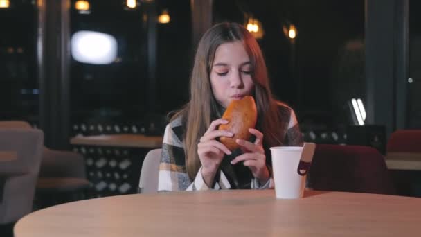 一个少女在吃面包 一个在咖啡馆里的女孩在晚上吃面包 快餐概念 小孩吃面包 高兴地咬面包 — 图库视频影像