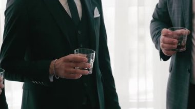 Erkek ellerinin viski, konyak ve brendi bardaklarını tuttuğu yakın plan. Takım elbiseli bir grup iş adamı ellerinde viski bardakları.