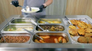 Bir kantin çalışanı tabağa bir porsiyon pirinç ve haşlanmış ciğer koyar. Tepsilerde çeşit çeşit yiyecekleri olan bir kantin şefi. Fabrikada kantin, çalışanlar için yemek.