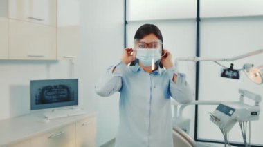 Diş Sağlığı Profesyoneli Randevuya Hazırlık, diş hekimi hasta etkileşiminden önce yüz kalkanı ve maskeyi ayarlıyor.