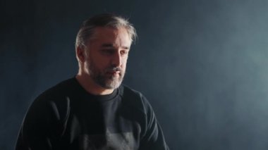 Karanlık Oda 'da Gri Saçlı Düşünceli Adam, Gri saçlı, sakallı, siyah gömlekli, orta yaşlı düşünceli bir adamın portresi.