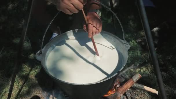 屋外の大きなポットで調理し 開放的な火の上に大きな鍋で木のスプーンで攪拌する人 — ストック動画
