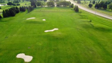 Ağaçlar, çalılar ve oyuncularla birlikte golf sahasının havadan görünüşü. Eğilirken golf sahasında uçmak, delikleri göstermek.