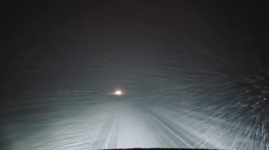 Gece yolundaki kar fırtınası, tek bir arabanın farları yoğun bir kar fırtınasının içinden geçiyor.