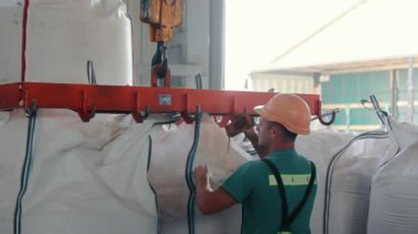 İşçi Crane 'den Depo' daki ağır çuvallara. Depo işçisi güvenlik teçhizatıyla büyük çuvalları taşımak için bir vinç kullanıyor..