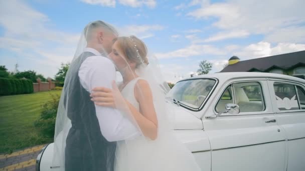 ブライダル ヴィンテージカーの近くに抱擁 結婚式の日にクラシックカーに愛情あふれる抱擁を分かち合う花嫁とグルーム — ストック動画