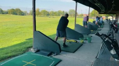 Golf antrenmanı yapan golf sahasında golf oynayan bir golfçü arka planda başkaları varken vuruşunu mükemmelleştiriyor.