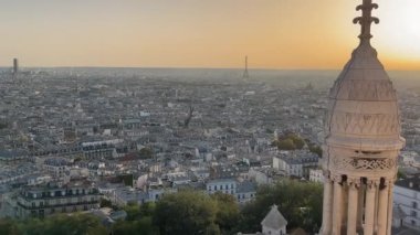 Paris 'te Eyfel Kulesi Manzarası ile Günbatımı, Paris şehri altın günbatımı ışığıyla yıkandı, uzaktaki Eyfel Kulesi ve süslü bir kulenin ayrıntılı önplanı yer aldı.