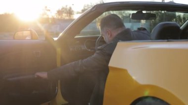 Günbatımında üstü açık bir arabayla Sunset Drive güzel bir günbatımında üstü açık bir arabanın kapısını açan adam.