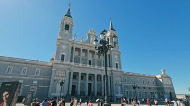 İspanya, Madrid 29.11.2024 Almudena Katedrali - Iconic Madrid Tarihi Eserleri, Almudena Katedrali 'nin heybetli cephesi, önplanda gezinen ziyaretçiler, açık mavi bir gökyüzünün arka planına karşı