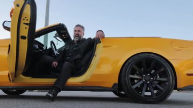 Sarı Cabrio 'da dinlenen olgun bir adam, sakallı, rahat, olgun bir adam üstü açık sarı bir arabada oturuyor ve eğleniyor.