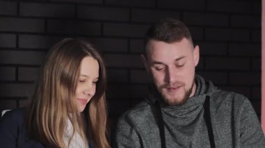 Tabletli çift, bir erkek ve bir kadın kapalı mekan aydınlatmasının ışıltısıyla aydınlanan tablet ekrana bakarken yakın ve kişisel bir anı paylaşırlar.