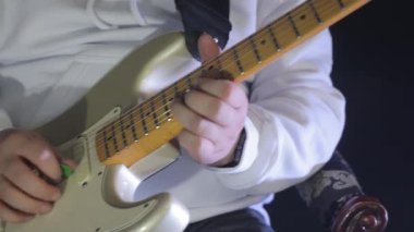 Beyaz kapüşonlu gitarist, elektro gitar çalıyor, yakın plan müzisyen elleri penayla elektro gitar tıngırdatıyor.