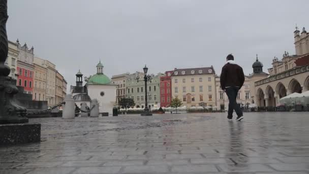 男人走过克拉科夫主广场 看到一个男人在阴天独自走过克拉科夫历史上著名的主广场上潮湿的鹅卵石 — 图库视频影像