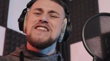 Tutkulu Erkek Vokalist Kayıt Şarkısı, bir ses kayıt stüdyosunda, mikrofon ve kulaklıkla tutkuyla şarkı söyleyen genç bir erkek şarkıcı.