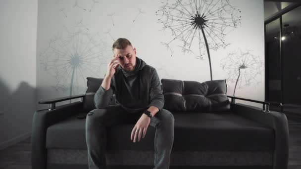 一个情绪低落的人坐在沙发上 一个沉思的人坐在一间时髦房间的灰色沙发上 陷入沉思 — 图库视频影像