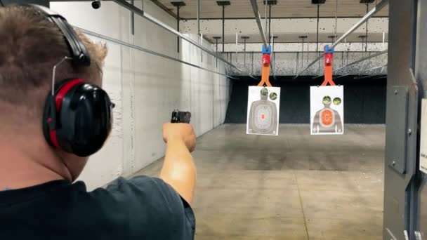 屋内射撃範囲で実践する男 屋内範囲での射撃スタンスに焦点を当てた男 ターゲットを目指して — ストック動画