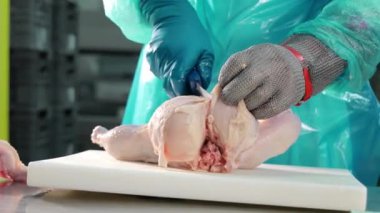 Ham Tavuğu Pişirmeye Hazırlayan Kasap koruyucu eldivenler giymiş uzman kasap beyaz kesim tahtasındaki çiğ tavuğun kemiklerini çıkarıyor.