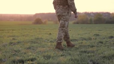 Kırsal bölgedeki askeri varlıklar gün batımında yeşil bir tarlada yürüyen yalnız bir asker hazır olmayı ve tetikte olmayı simgeliyor.