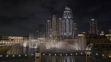 Dubai - Birleşik Arap Emirlikleri 01.05.2024 Timelaps Olağanüstü Çeşme Şovu Dubai şehir merkezinde. Büyüleyici bir çeşme, aydınlatılmış gökdelenlerin arkaplanına bakan geceyi aydınlatıyor.