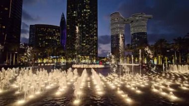 Urban Park 'taki Gece Su Fıskiyeleri, Şehir parkında gece fıskiyeler parlak bir şekilde aydınlatılıyor, modern binalar arka planda çarpıcı bir kontrast oluşturuyor.