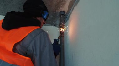 Güvenlik teçhizatı takan odaklanmış bir inşaat işçisi inşaat sahasındaki bir boruya kaynak makinesi kullanıyor ve etrafında kıvılcımlar uçuşuyor..