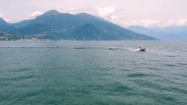 Como Gölü 'nü aşan sürat teknesi Como Gölü' nün sakin sularını kesiyor. Görkemli bir dağ arkaplanı ve bulutlu gökyüzü ile İtalyan manzarasının heyecanını ve güzelliğini vurguluyor.