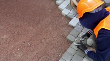 İşçi Pavement Blokları, turuncu güvenlik teçhizatı içinde bir işçi dikkatle birbirine kenetlenmiş kaldırım bloklarını yeni hazırlanmış taban tabakasına yerleştiriyor.