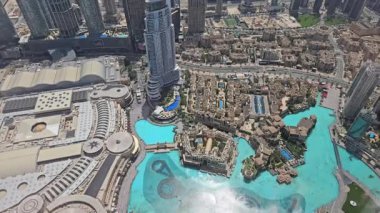 Modern mimari, yüksek binalar ve canlı mavi yapay göl içeren hareketli şehir manzarasının çarpıcı bir hava görüntüsü.