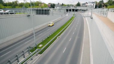 Az trafiği ve üst geçidi olan bir otoyol. Otoyolda trafik açık, şehir ortamında üstgeçidin altından geçen arabalar var.