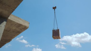 İnşaat alanındaki tuğla paletini kaldıran bir vinç inşaat alanındaki tuğla paletini havaya kaldıran bir vinç bulutlu açık mavi bir gökyüzüne karşı kurulmuş..