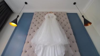 Şık bir yatak odasında yatağın üstünde asılı gelinlik şık bir yatak odasında düzgün yapılmış bir yatak başlığının üstünde asılı gelinlik..