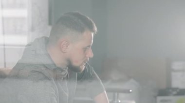 Modern bir odada, derin düşüncelere dalmış bir adam, derin düşüncelere dalmış, yumuşak, dağınık bir ışıkla modern odayı dolduruyor..