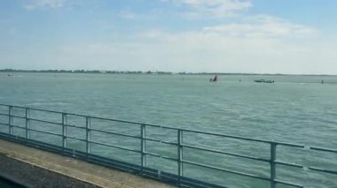 Venedik gölüne bakan bir köprüden, sakin suların açık mavi gökyüzünün altında uzandığı Venedik gölüne bakan bir köprüden çekilen huzurlu bir görüntü.