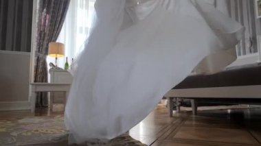Gelin beyaz bir bornozla pencereye gider. Dalgalı beyaz elbiseli bir gelin zarif bir şekilde dekore edilmiş bir odada döner, pencereden süzülen yumuşak ışıkla.