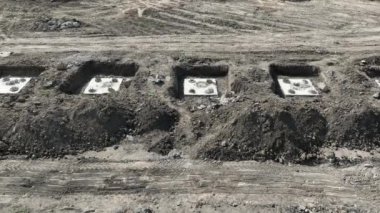 İnşaat alanı temelleri yeni kazılmış toprakta. Beton temellerden yükselen güçlendirilmiş çelik çubuklarla toprağı kazan birkaç dikdörtgen temel çukurunu gösteren bir inşaat sahası