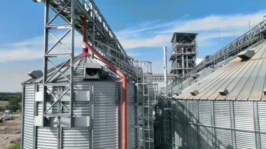 Metal yapıları ve mavi gökyüzü olan tahıl deposu. Metal geçitler ve boru hatlarıyla birbirine bağlı büyük metal siloların bulunduğu modern bir tahıl depolama tesisi.