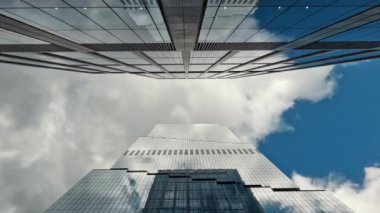 Bulutlu gökdelenlere karşı modern gökdelenlerin yukarı bakan görüntüsü, parçalı bulutlu gökyüzüne uzanan modern cam gökdelenlerin çarpıcı perspektifi.