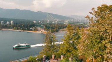 Lions Gate Köprüsü Vancouver. Sürat teknesi dağ zeminli büyük bir asma köprünün altından geçiyor.