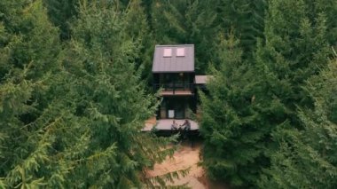 Ormanda, Noel ağaçlarının arasında, modern bir ahşap ev. İki adam terasta çay içiyor. Ormanda, inanılmaz doğanın ortasında rahat bir ev..