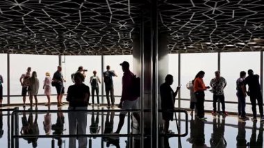 Dubai OAE 20.10.2024 Burj Halife Gözlem Güvertesi 'nde turistlerin siluetleri, tavanı desenli ve yansımaları parlak gün ışığına karşı dramatik ve sürükleyici bir sahne yaratıyor..