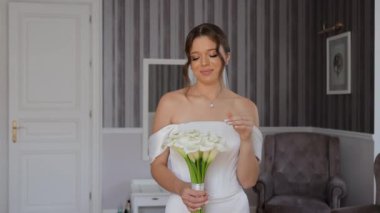 Zarif Oda 'da Gelin Tutma Buketi, beyaz omuzsuz gelinlik içinde güzel bir gelin bir buket zambak tutuyor.