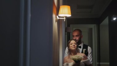 Dim Hollway 'de kucaklaşan romantik çift, loş bir koridorda yeni evli çift, damat gelini arkadan kucaklarken elinde bir buket çiçek tutuyordu..