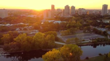 Chicago parkı ve gün batımında binalar. Gün batımında ağaçlar, binalar ve şehir ve gökyüzünü dolduran sıcak turuncu bir parkın havadan görüntüsü.