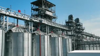 Mavi gökyüzüne karşı metal yapıları olan sanayi tahıl ambarları. Karmaşık yapılar ve boru hatlarıyla birbirine bağlı birçok metal silosu olan büyük ölçekli bir sanayi tahıl depolama tesisi.