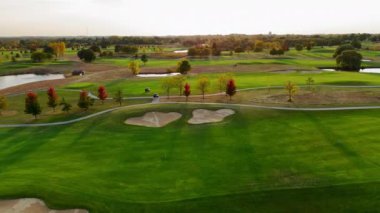 Güz Ağaçlı Manzaralı Golf Sahası, Kum tuzaklarının, canlı sonbahar ağaçlarının, göletlerin ve yumuşak güneş ışığı altında yeşil çayırların bulunduğu yemyeşil bir golf sahasının havadan görünüşü.