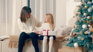 Noel kutlamalarında aile görüntüsü. Anne ve iki kız Noel çelenkleri ve kırmızı bir kurdeleyle süslü merdivenlerde oturarak neşeli bir videonun tadını çıkarıyorlar.