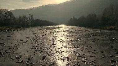 Sunlit Nehri Vadi 'de akıyor. Sakin bir nehir, bulutlu bir gökyüzünün altında ağaçlar ve tepelerle çevrili sakin bir vadiden akan güneş ışığını yansıtıyor.
